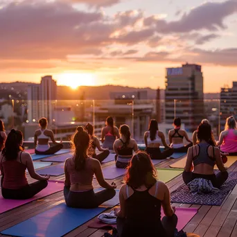 Participants doing yoga on a rooftop at sunrise with city views - Image 1