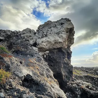 Wildly shaped volcanic rock cliffs with a bright cloudscape and rainbow. - Image 1