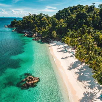 Aerial view of a secluded tropical beach with white sand, clear waters, and surrounding palm trees. - Image 1