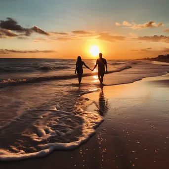 Couple walking along the beach during a vibrant sunset. - Image 1