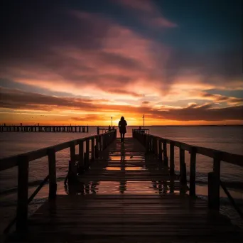 Silhouette of a person watching the sunset on a pier by the ocean - Image 1