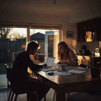 Couple discussing budget with laptop and papers in kitchen - Image 1