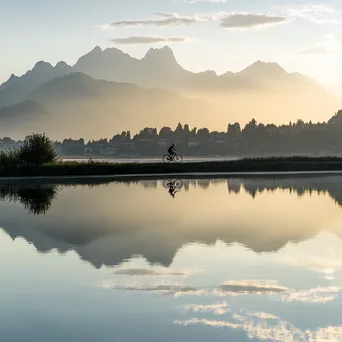 A cyclist riding near a lake with mountain reflections during sunset. - Image 3