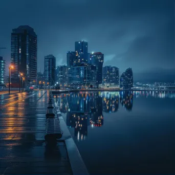 City waterfront promenade with buildings reflecting in calm waters and shimmering lights at night - Image 1