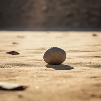 Single smooth stone placed on dry sand. - Image 1