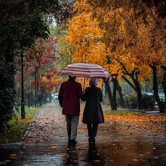 Elderly couple walking under a striped umbrella in autumn rain - Image 3