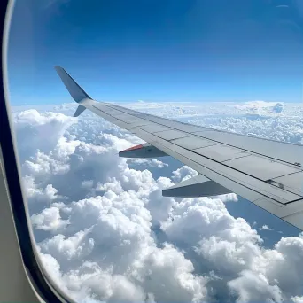 Aircraft wing and fluffy clouds in clear blue sky seen from airplane window - Image 1