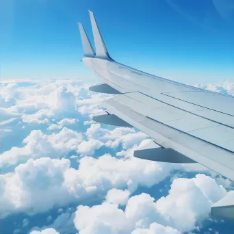 Aircraft wing and fluffy clouds in clear blue sky seen from airplane window - Image 2