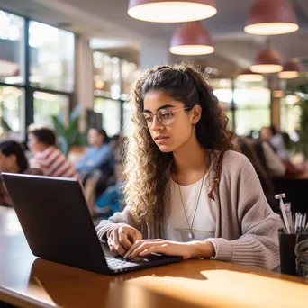 Student typing on a laptop at a desk in a library with natural light. - Image 1