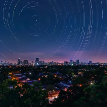 Star trails streaking across the sky above a vibrant city skyline - Image 2