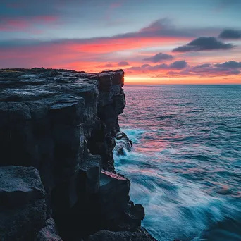 Black lava rock faces contrasting with a colorful sunset and ocean waves. - Image 1