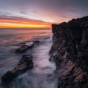 Black lava rock faces contrasting with a colorful sunset and ocean waves. - Image 2