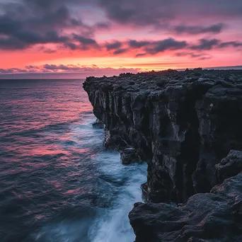 Black lava rock faces contrasting with a colorful sunset and ocean waves. - Image 3