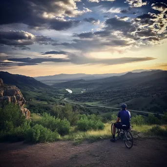 A lone cyclist resting at a mountain overlook during sunset. - Image 1