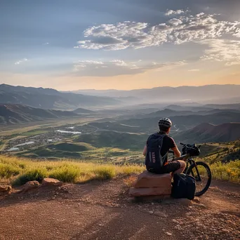 A lone cyclist resting at a mountain overlook during sunset. - Image 2