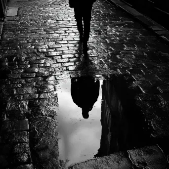 Artwork of a solitary figure reflected in a puddle on a rainy cobblestone street, in film noir style - Image 4