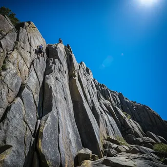 Climbers ascending a granite rock wall with a clear blue sky. - Image 1