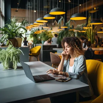 A woman on a phone call while typing on a laptop in a co-working space. - Image 4