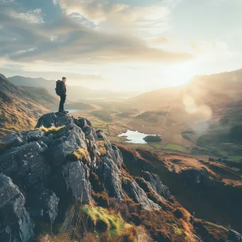 A hiker on a rocky cliff gazing over a sunlit valley - Image 1