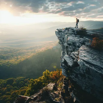 A hiker on a rocky cliff gazing over a sunlit valley - Image 4