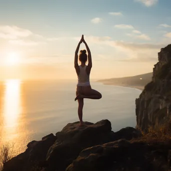 Woman practicing yoga on a cliff overlooking the ocean. - Image 1