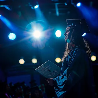 Graduate standing on stage holding diploma under bright lights - Image 3