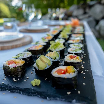 An elegant display of assorted vegan sushi rolls with garnishes on a slate board. - Image 1