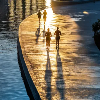 Diverse individuals jogging along a waterfront path at sunset. - Image 2