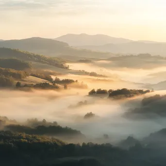 Misty valley landscape at dawn with sunlight breaking through fog - Image 1