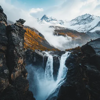 Waterfall falling into a rocky gorge with snow-capped peaks - Image 2