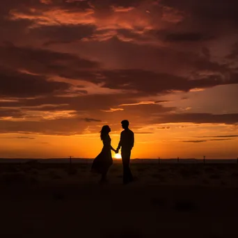 Couple holding hands silhouetted at sunset in black and white - Image 1