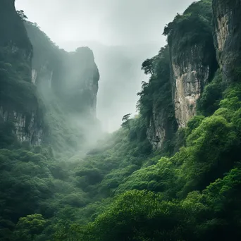 Sheer mountain cliff face surrounded by morning mist and greenery. - Image 1