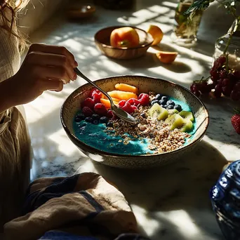 Individual preparing a smoothie bowl with fruits and granola - Image 1